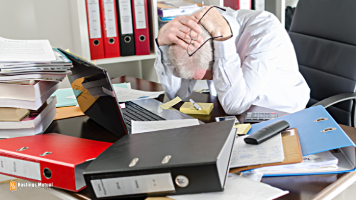 a business man with his head down on a desk piled with binders and papers