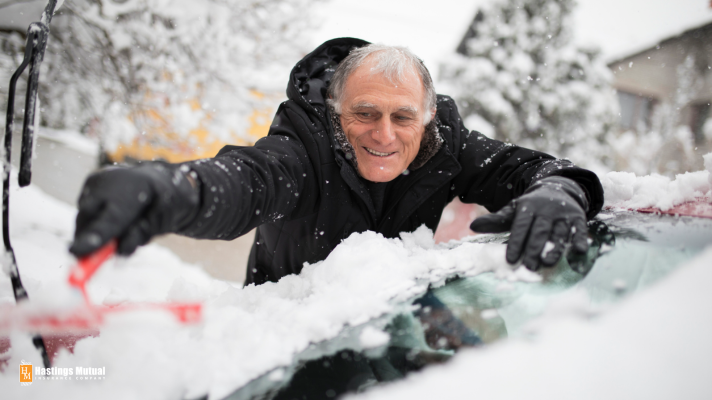 man cleaning snow off of car before winter driving